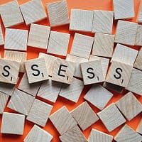 An orange background with Scrabble letters spelling out the word "assess"