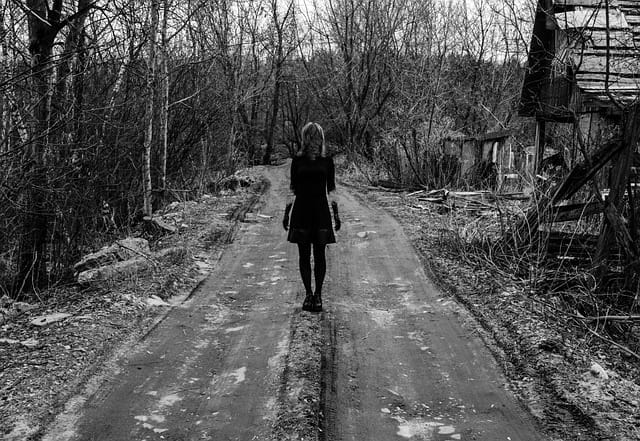 A creepy black and white image of a woman wearing a dress on a lonely road