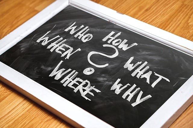 A chalkboard sitting on a table with the words "how, what, why, where, when, and how'